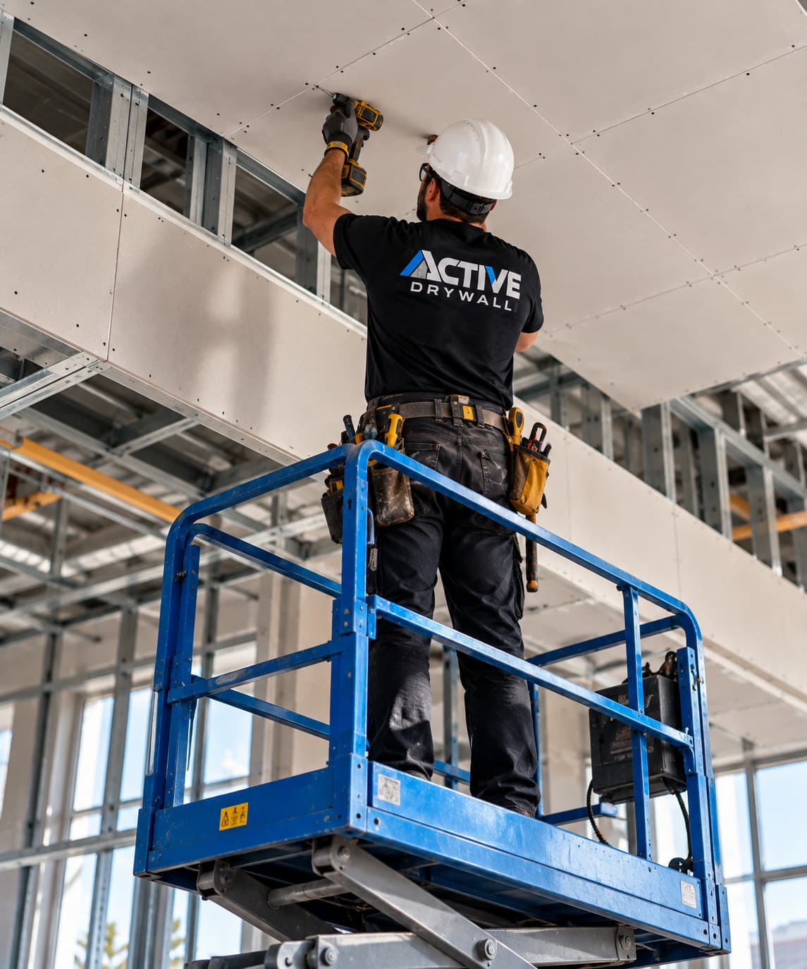 Active Drywall installer on a scissor lift fastening drywall to a high ceiling with a drill
