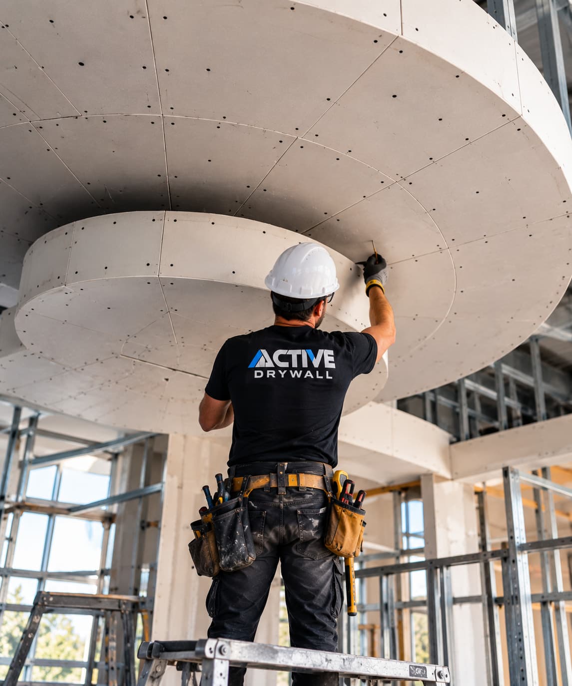 Active Drywall installer working on layered, curved drywall soffits on a ceiling