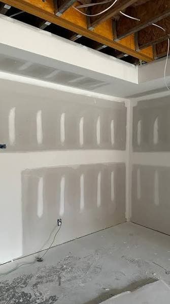 Drywall walls with coats of joint compound feathered over seams and fasteners in an unfinished room